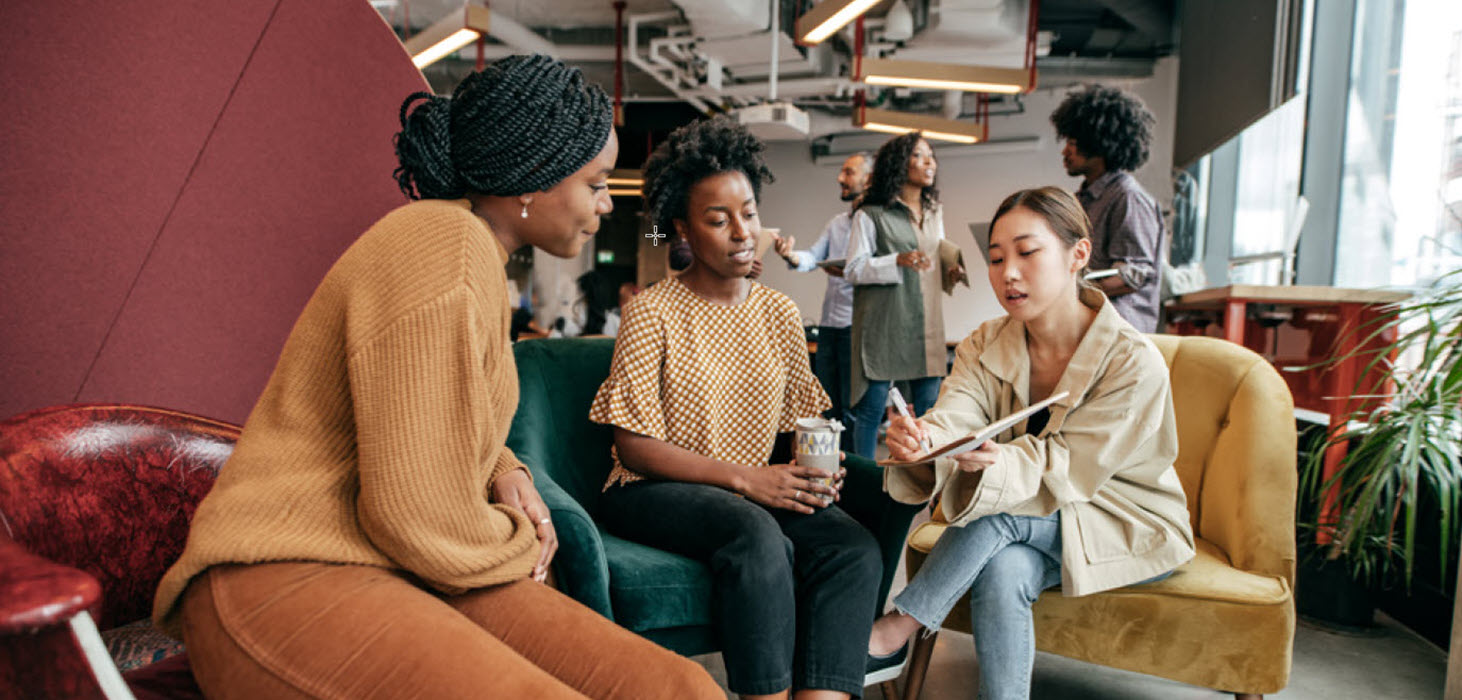 Three women sitting in arm chairs talking and looking at an ipad.