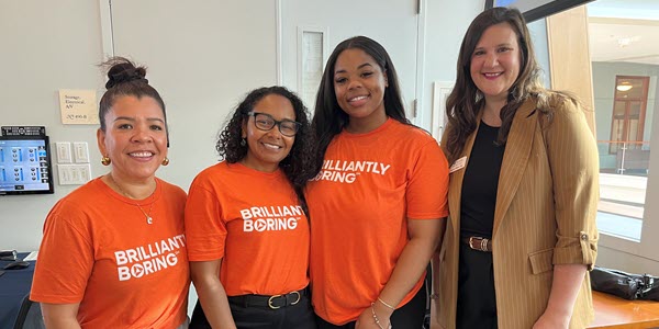 A group of PNC employees smiling at the camera wearing "Brilliantly Boring" shirts