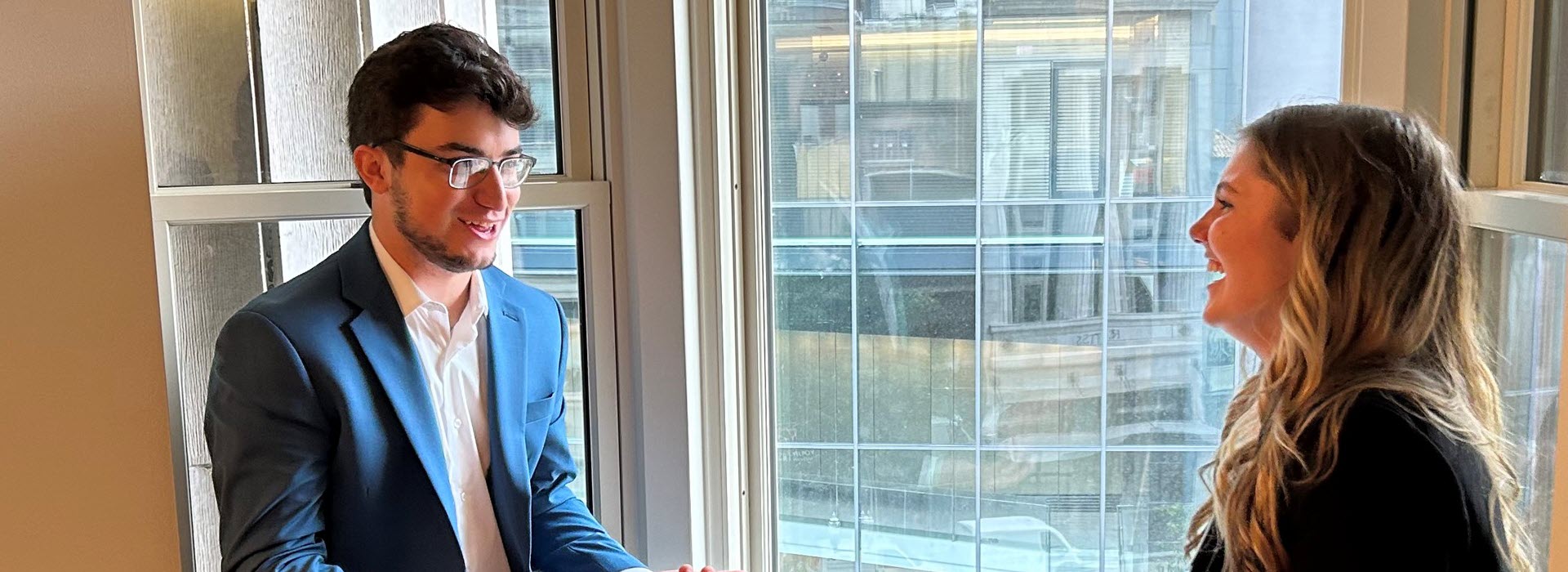 A campus recruiter speaking with a candidate in front of a window