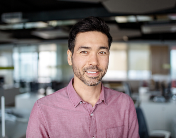 Headshot of a man wearing a light red polo shirt with a blurred office in the background.