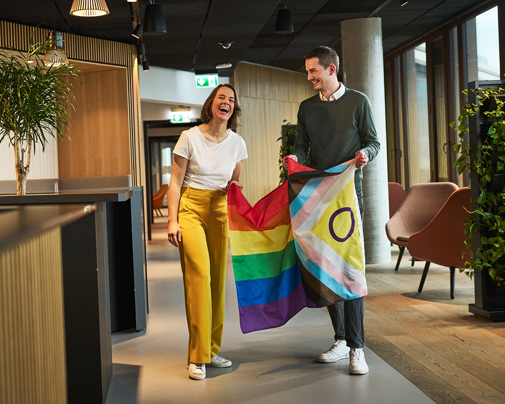 Zwei Mitarbeitende stehen zusammen und halten eine Pride Flag