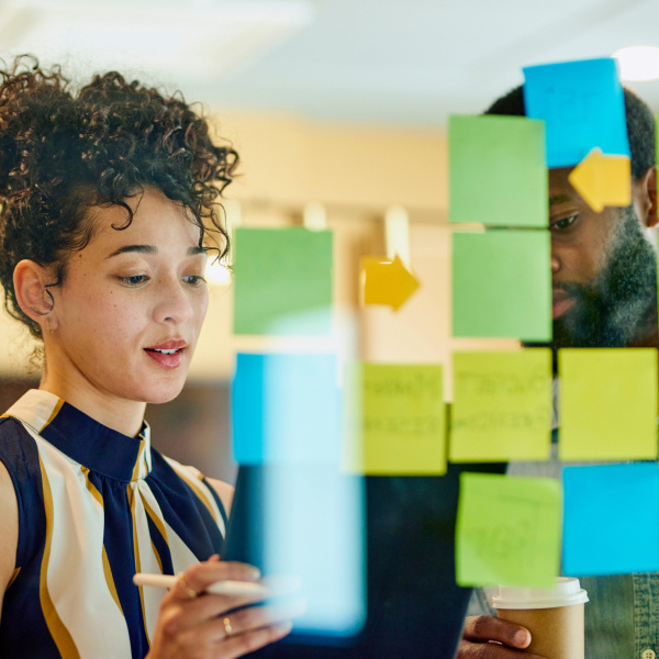 Man and a woman in front of a glass writing on sticky notes