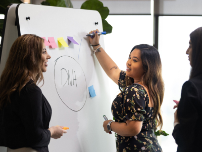 Three women around a whiteboard with DNA on it