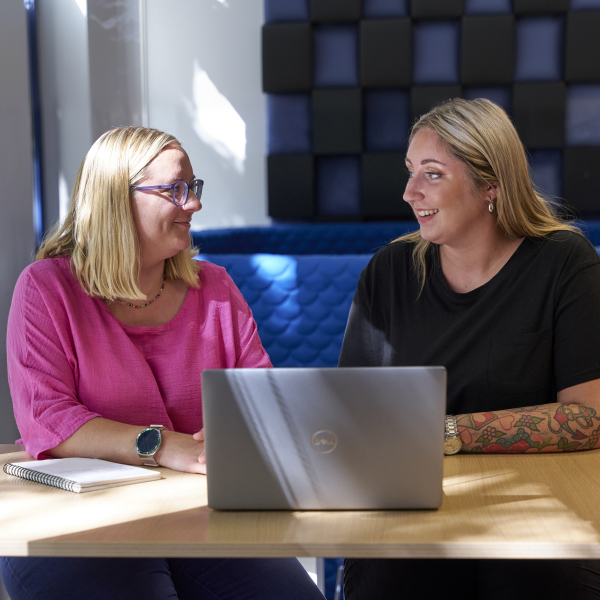 Two ladies sitting at a booth with a laptop