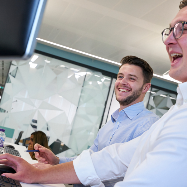 Two young men in shirts laughing at a screen