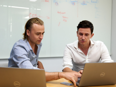 Two young men with laptops in front of whiteboard