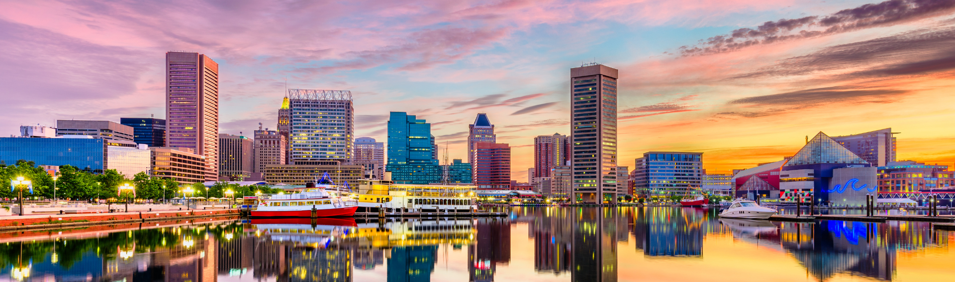 Colorful sunset over Baltimore’s Inner Harbor with boats docked and skyscrapers reflecting in the water