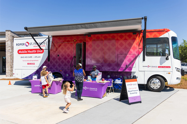Community mobile health unit bus with five people in the foreground on a sunny day