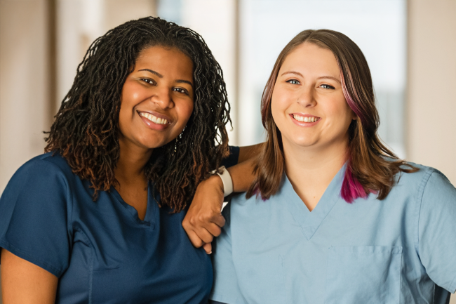 Two women in scrubs smiling in a hospital setting