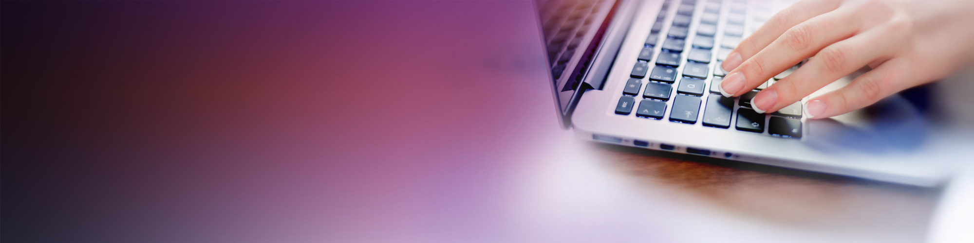 Close-up of a person's hand typing on a laptop keyboard, with a blurred gradient background transitioning from dark to light tones