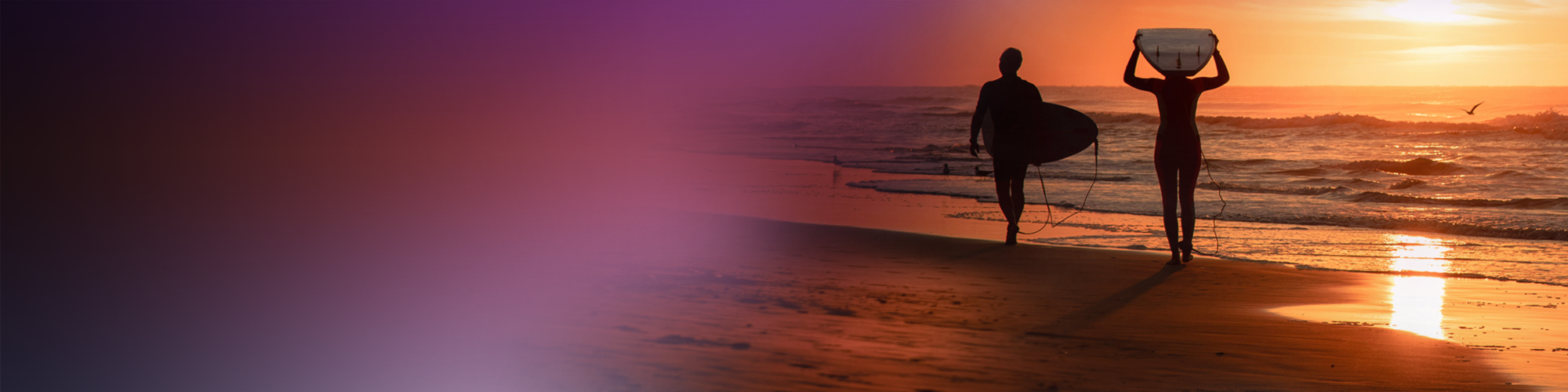 Two people carrying surf boards at dusk on the beach with a gradient from light to dark background