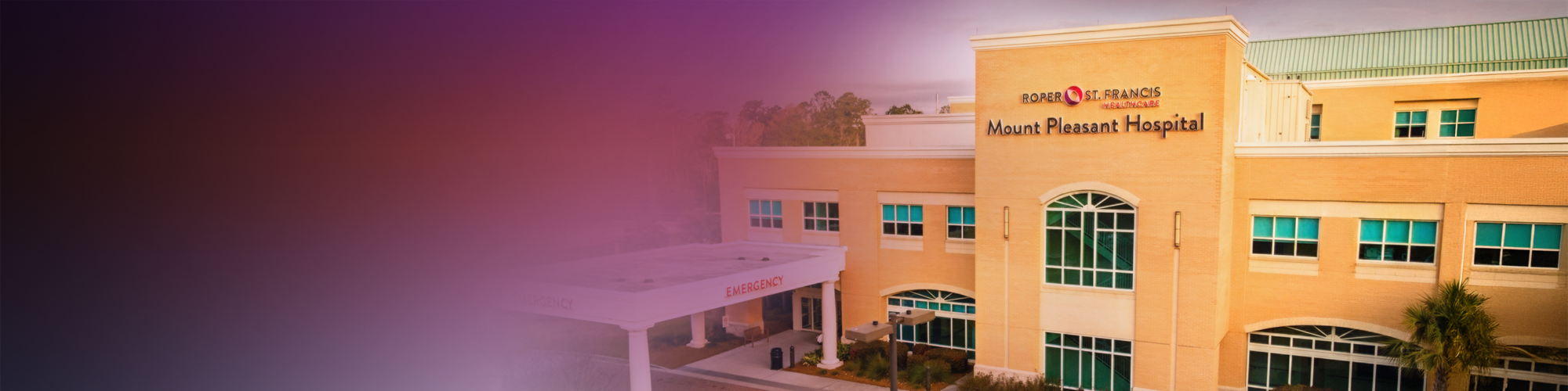 Exterior view of a tan building Mount Pleasant Hospital with a blurred gradient background transitioning from dark to light tones