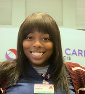 Smiling headshot of professional wearing scrubs and name tag with logo in background