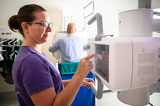 Woman with glasses using an imaging machine and a man in the background receiving the test