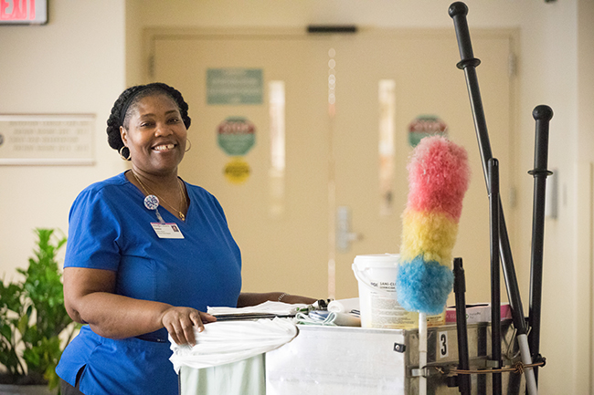 Woman smiling with name badge and cart of supplies in a hospital hallway
