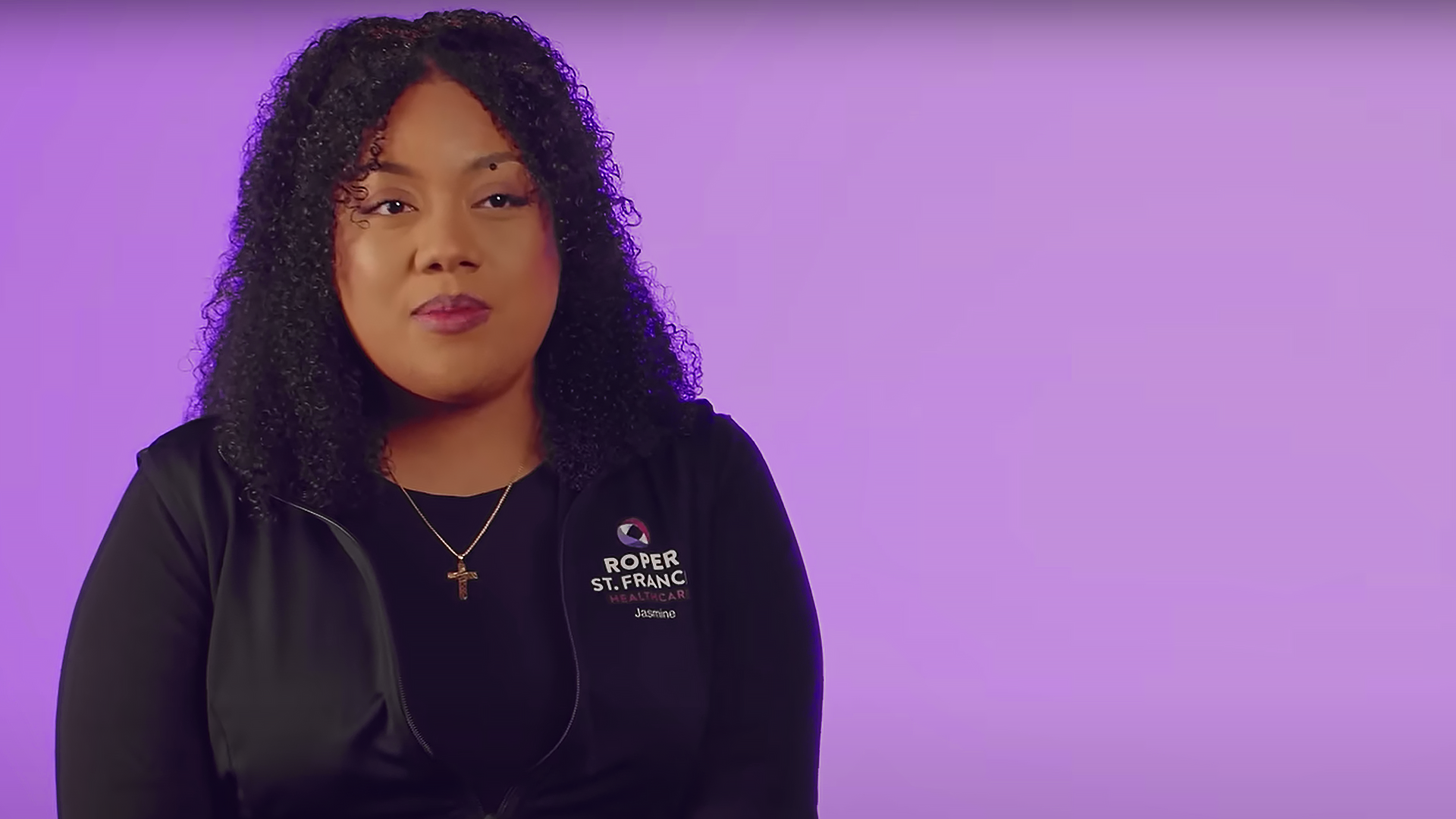 Woman wearing logo jacket talking to camera with a purple background