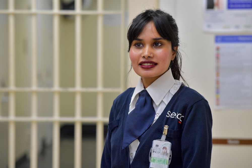 A woman in a blue cardigan with a Serco logo on