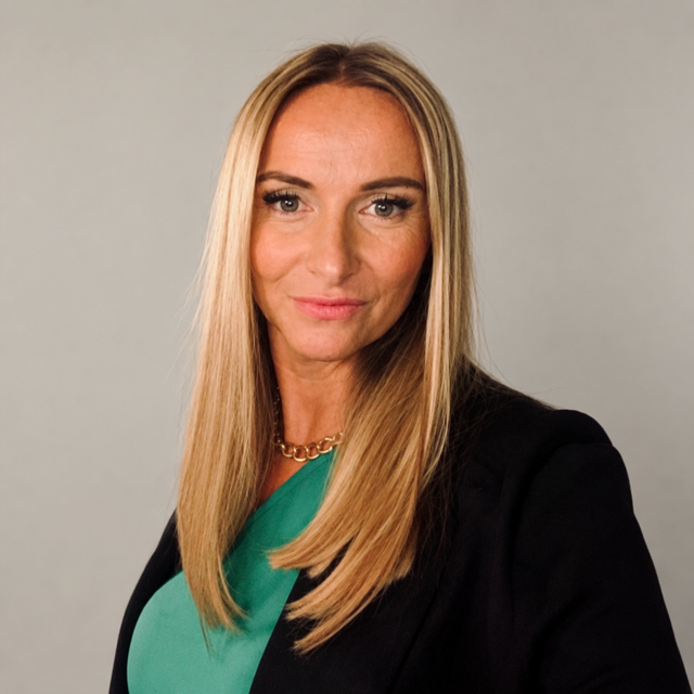 A woman in a green top and black blazer, looking into the camera