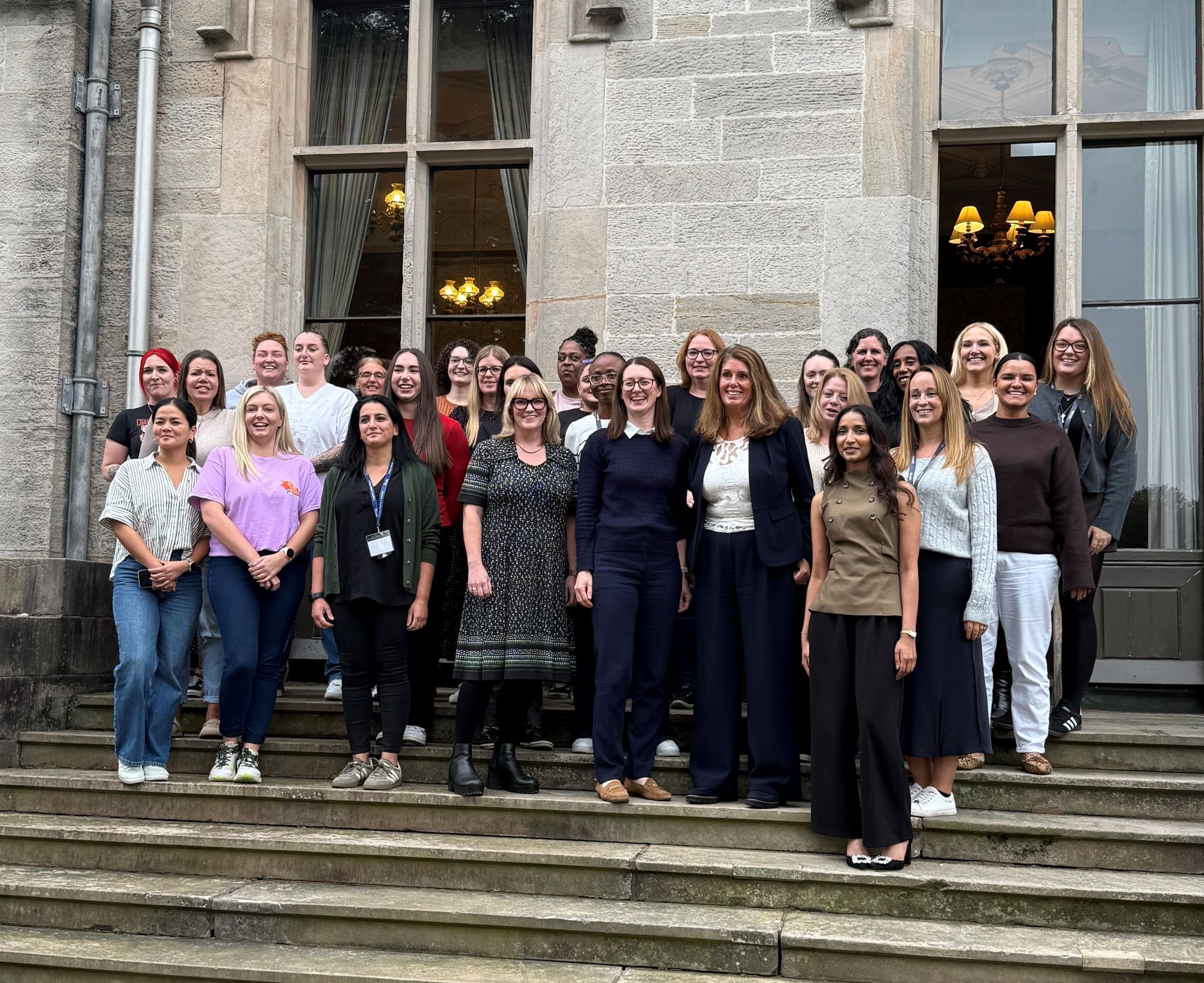 A group of women standing on steps and smiling - they are the first cohort of women to undertake the Serco Empower programme for female leaders.
