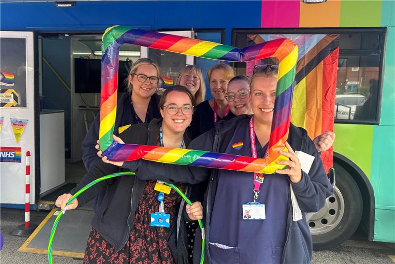 A group of women with a large rainbow-striped inflatable photo frame around them