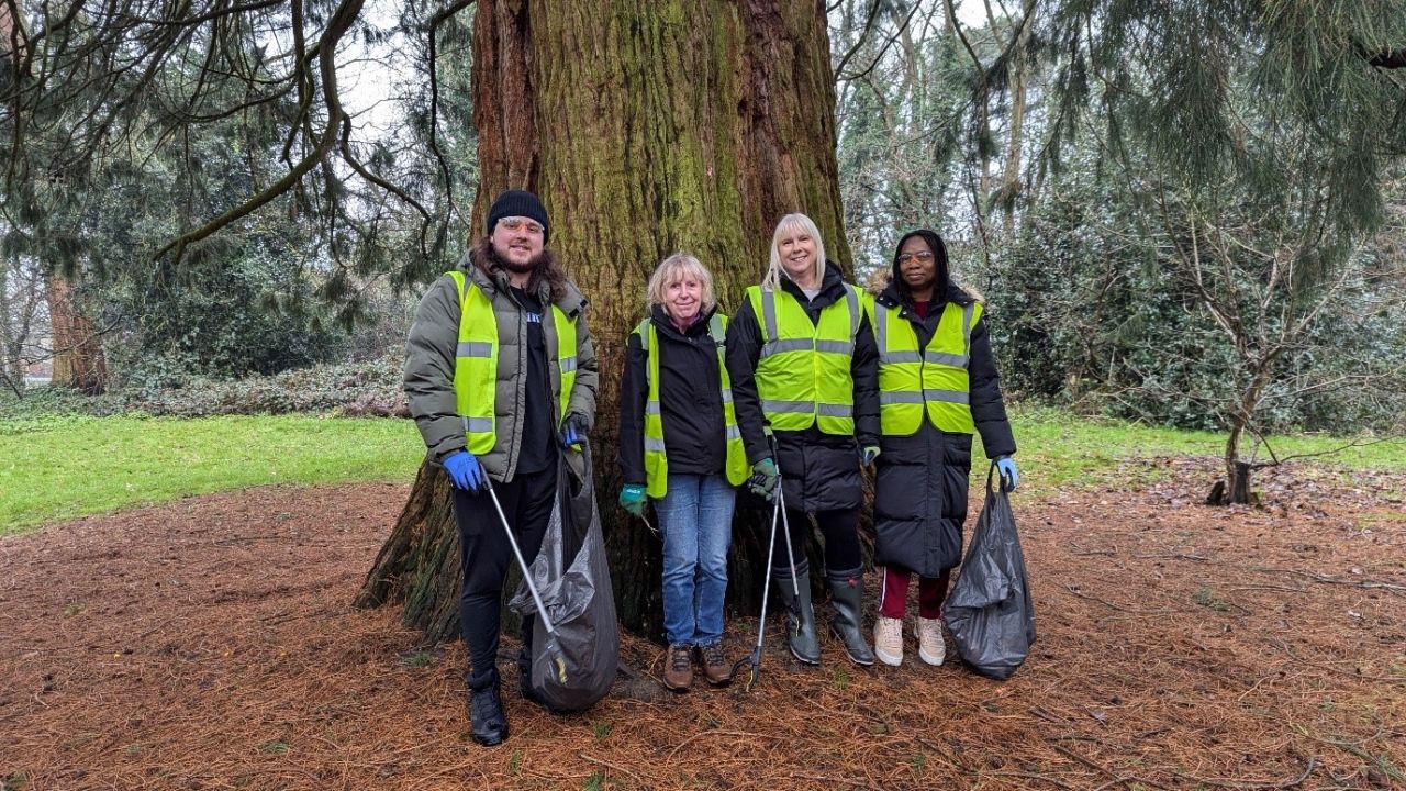 Four people stood in front of a tree with high vis jackets and litter pickers.
