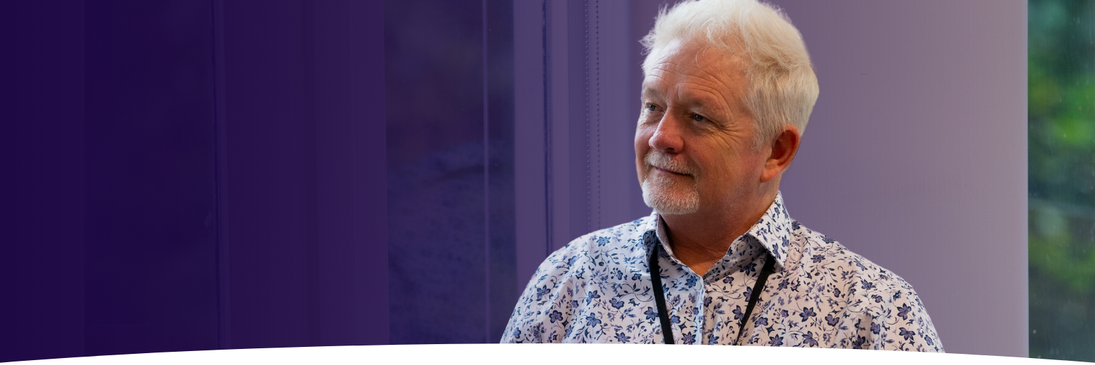 Man with white hair in a floral shirt with a lanyard on