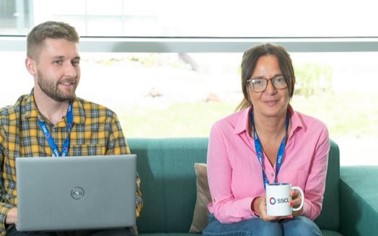 Two of our colleagues sitting together on a sofa. One is holding a branded SSCL mug