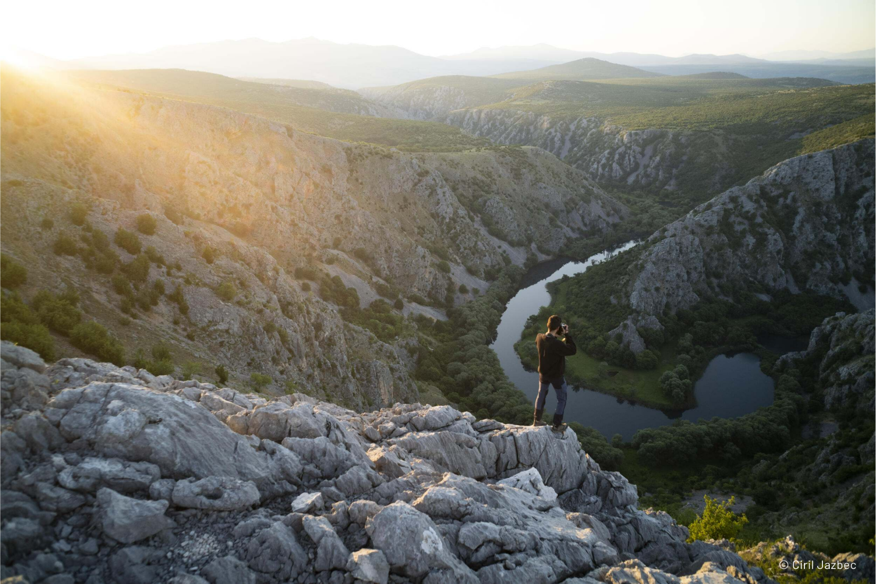 A person standing on a rock looking at a river