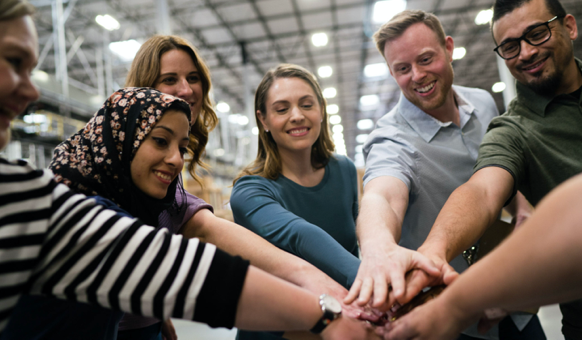 Group of people smiling and putting their hands together in the middle.