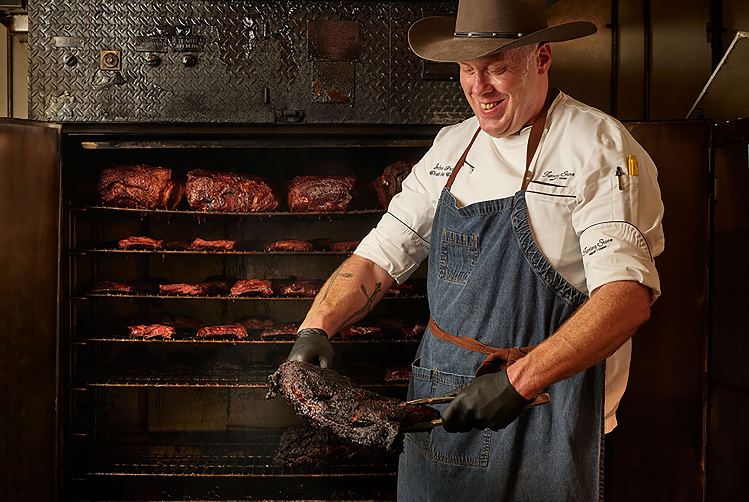 Tin Rooster Honky Tonk pitmaster is basting a piece of meat to go on the grill. 