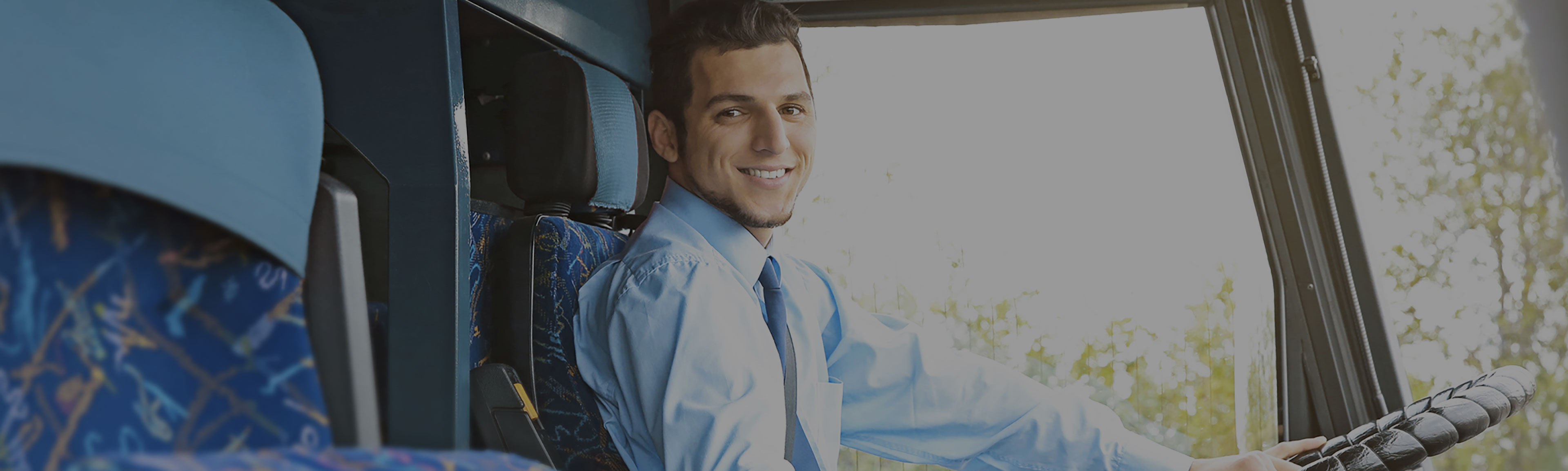 A team member is smiling for a picture from behind the wheel of a shuttle. 