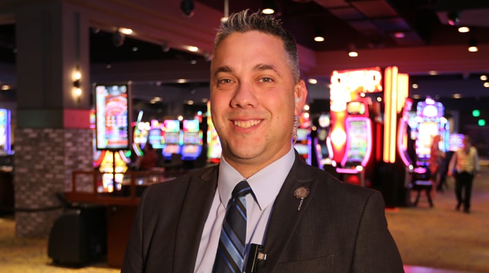 A team member smiles for the camera with the glowing lights of one of Turning Stone Enterprises' casinos in the background. 