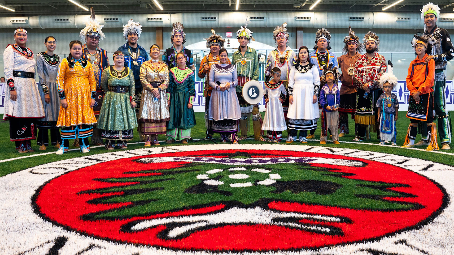 Oneida Indian Nation members dressed in their traditional clothes and standing around a rug designed to look like the Nation's emblem. 