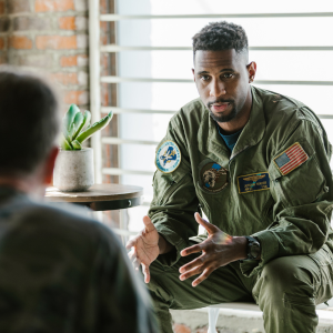 Hombre en uniforme militar conversando con otro hombre frente a él.