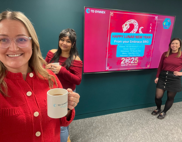 3 co-workers smiling and standing in front of a display screen that says "Happy Lunar New Year"