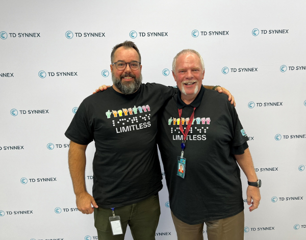 2 male co-workers smiling while wearing Limitless shirts in front of a TD SYNNEX backdrop.