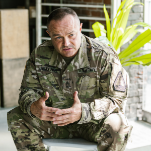 Man in military uniform sitting on a stool and speaking