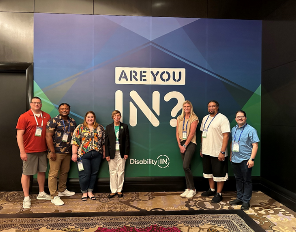 7 co-workers standing in front of a DisabilityIn sign that says "Are You In?"