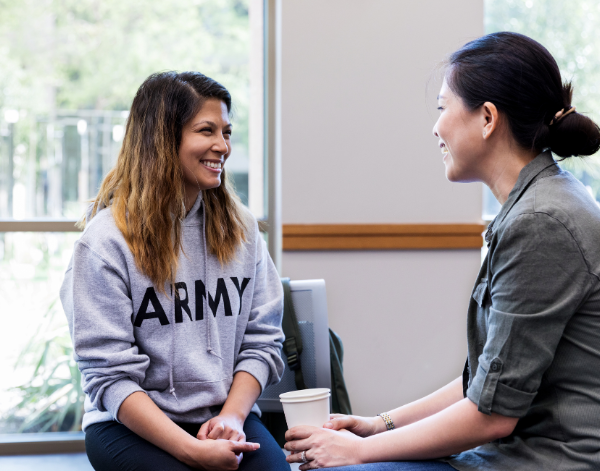 2 women chatting in an office. One of the women is wearing a sweater that reads "ARMY".