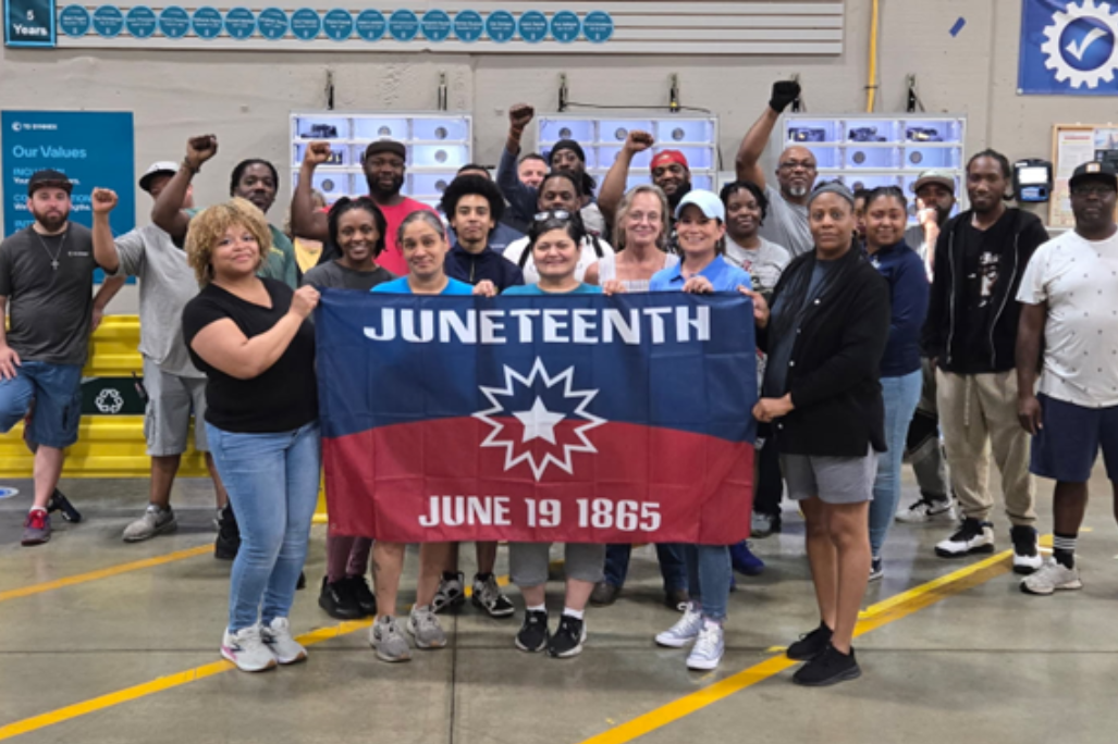 Co-workers at a logistics center holding a flag celebrating Juneteenth
