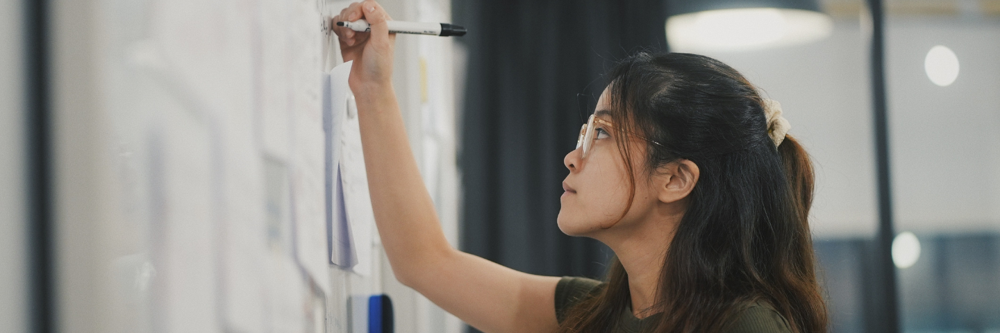 Young woman with glasses writing on a whiteboard.