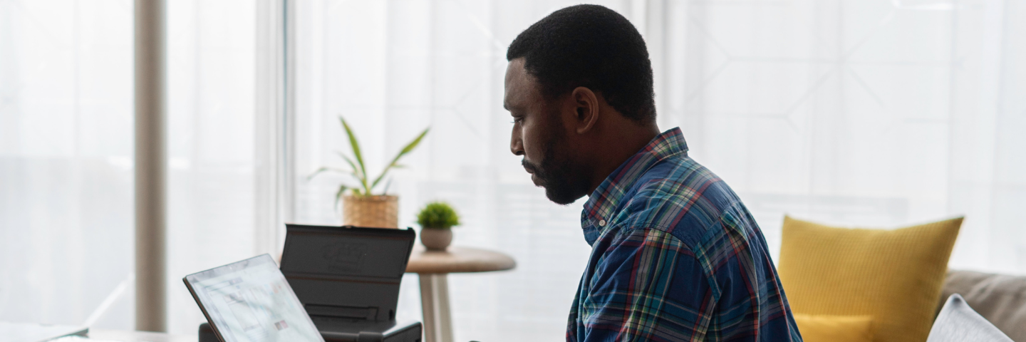 Man in flannel shirt sitting in an at-home office, looking at tablet computer.