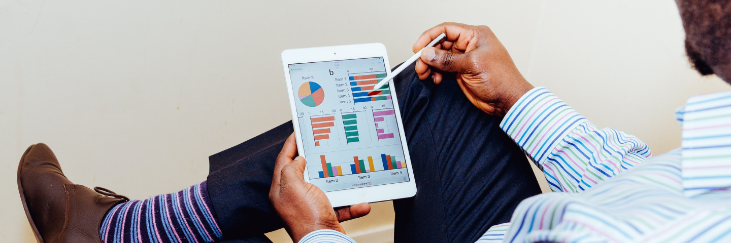 Man in business attire pointing to tablet computer in his lap with a pen.