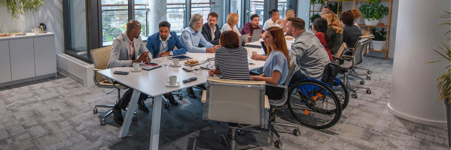 16 coworkers in an office setting, sitting at a large conference table.