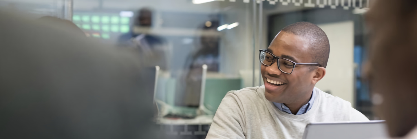 Jeune étudiant à lunettes assis dans un bureau, souriant avec son ordinateur devant lui.