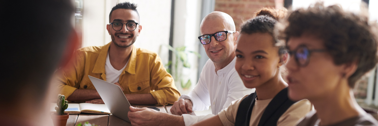 5 collègues souriants assis à une table dans un bureau.