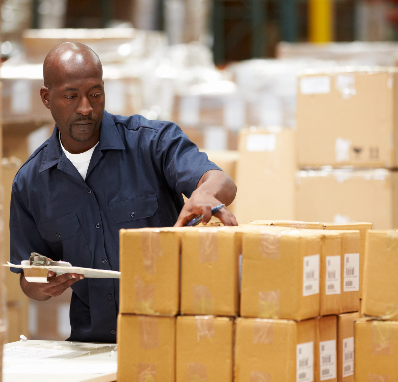 Man holding clipboard while examining packages in a warehouse.