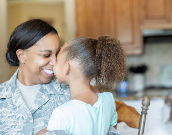 Mom in military uniform smiling while holding her daughter in the kitchen.