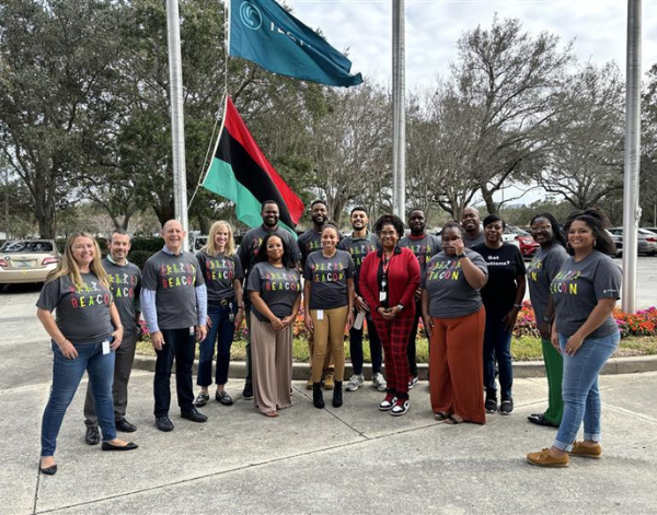 17 coworkers smiling at a Pan-African flag raising.