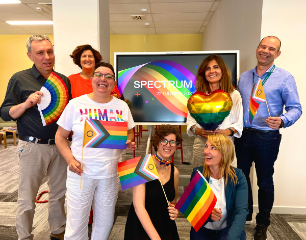 7 employees smiling in front of a 'Spectrum' sign holding pride flags.